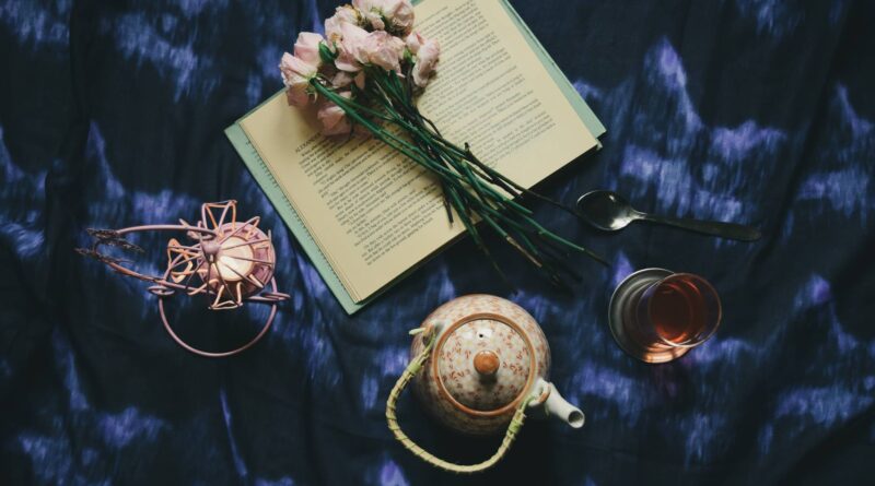 opened book with flowers placed on silk near teapot