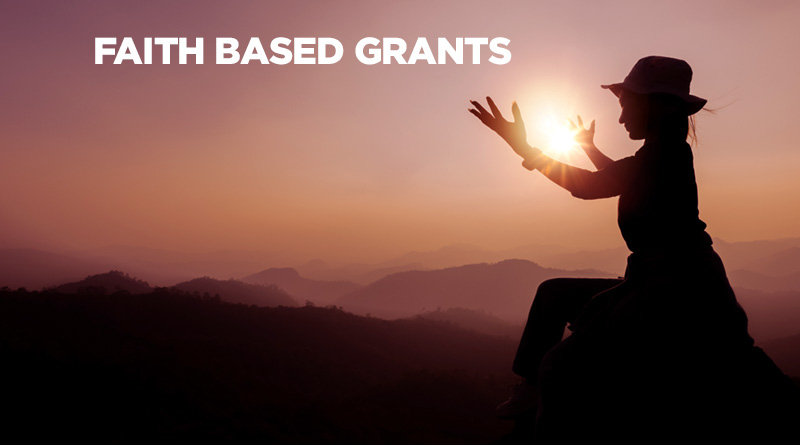 Woman sitting in the mountains at dusk. An optical illusion makes it seem as though she is holding the sun in her hands. Caption reads: Faith-Based Grants.