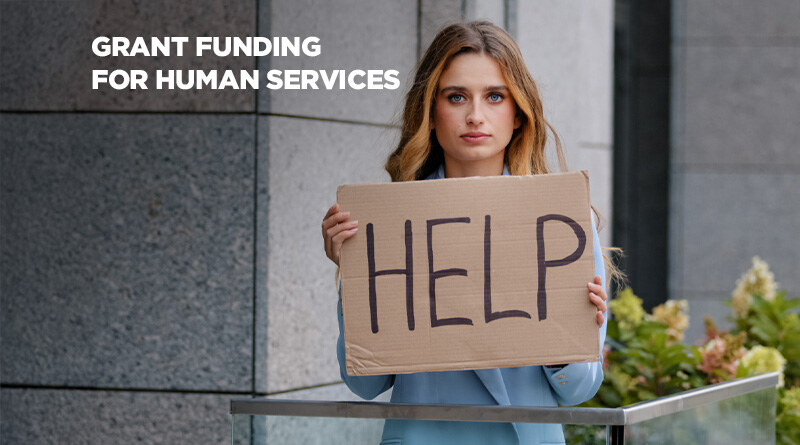 Woman holding a sign that says HELP. Caption reads: Grant Funding For Human Services..