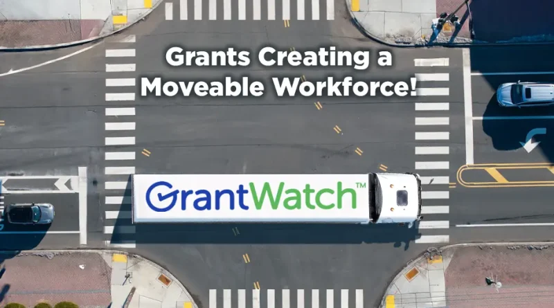 Aerial view of a large white truck driving through a city intersection. The truck trailer displays the GrantWatch logo, and above the truck, bold text reads “Grants Creating a Moveable Workforce!” Crosswalks, streets, and a few cars surround the intersection.