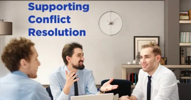A group of three men in business attire sit around a table in a modern office, engaged in a friendly discussion. One man gestures with his hands while the others listen and smile. Laptops and a tablet are on the table. On the wall behind them is a clock and shelves with books. Blue text on the left reads “Supporting Conflict Resolution.”