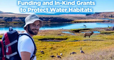 A smiling hiker wearing a hat and backpack stands near a river surrounded by grasses, elk, and waterfowl, with the text “Funding and In-Kind Grants to Protect Water Habitats” displayed over the landscape.