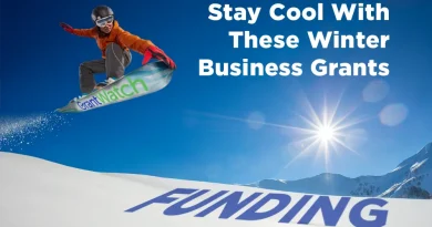 A snowboarder jumps across a snowy mountain slope on a snowboard labeled “GrantWatch,” with the word “FUNDING” printed in large letters on the snow and the text “Stay Cool With These Winter Business Grants” in the sky above.