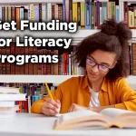 Young woman studying at a library table, writing in an open book with stacks of books nearby and bookshelves behind her, with the text “Get Funding for Literacy Programs” displayed on the image.