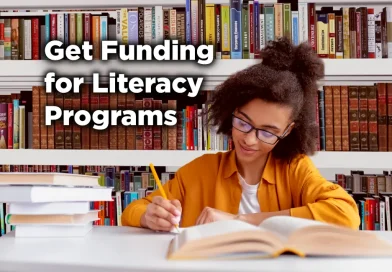 Young woman studying at a library table, writing in an open book with stacks of books nearby and bookshelves behind her, with the text “Get Funding for Literacy Programs” displayed on the image.