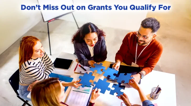 Team of colleagues assembling blue puzzle pieces at a meeting table beneath the headline “Don’t Miss Out on Grants You Qualify For.”