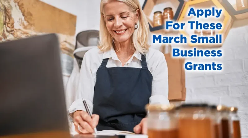 Woman small business owner wearing an apron works on a laptop and writes in a notebook at her shop counter, with text overlay reading “Apply For These March Small Business Grants.”
