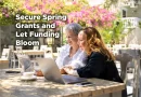 Two entrepreneurs sit outside at a stone picnic table, smiling and looking at a laptop. It's Spring and there are pink blossoms all around. Caption reads: Secure Spring Grants and Let Funding Bloom."