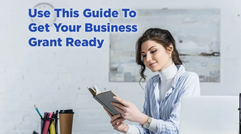 Professional woman at a desk reading a notebook beside a laptop and office supplies, with text overlay: “Use This Guide To Get Your Business Grant Ready.”