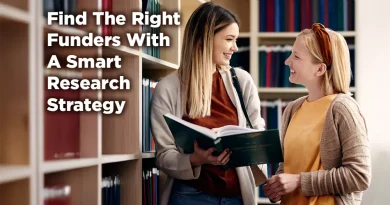 Two women smiling and reviewing a book in a library aisle, with shelves of binders in the background and text reading “Find the Right Funders With a Smart Research Strategy.”