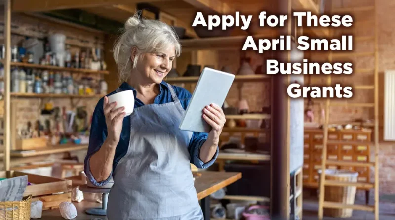 Smiling small business owner in a workshop apron holding a tablet and coffee mug, standing in a creative studio space, with text overlay reading “Apply for These April Small Business Grants.”