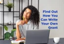 A woman, sitting in front of her laptop, looking whimsically up to her right, lost in thought. She ponders the caption: " Find Out How You Can Write Your Own Grant."