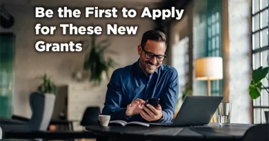 Man sits at his laptop but typing on his phone and smiling. The caption reads: Be the First to Apply for These New Grants