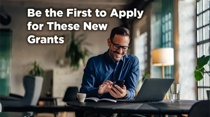 Man sits at his laptop but typing on his phone and smiling. The caption reads: Be the First to Apply for These New Grants