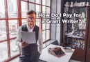 A man stands in his office at work. He is holding a completed grant application and smiling while the application is cleverly reflected in the glasses he's wearing. A typewriter sits on the desk behind him and the book-laden bookcase suggests he's an academic. The caption poses a question: How Do I Pay foe a Grant Writer?