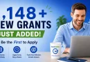 Promotional graphic for GrantWatch showing a smiling man working on a laptop at a desk. Large blue text reads “1,148+ NEW GRANTS JUST ADDED!” with a green banner underneath saying “JUST ADDED!” Additional text says “Be the First to Apply.” Three icons at the bottom highlight features: “New Grants Added Daily,” “Apply Early. Stay Ahead.” and “Fund Your Mission. Create Impact.” A branded coffee mug with the GrantWatch logo sits beside the laptop against a blue office-style background.