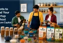 Three people in a pet food startup kitchen and testing lab prepare dog food recipes while interacting with two dogs. Shelves of ingredients, measuring tools, bowls of food, and packaged pet food products are displayed on a worktable. Large text on the left reads, “Grants to Fund Your Startup Without Venture Capital,” with the GrantWatch logo in the upper-right corner.