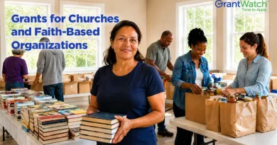 Volunteers and community members at a church-based outreach program sort books and pack grocery bags in a bright community room. A woman in the foreground holds a stack of books while others prepare donations. Text on the image reads: "Grants for Churches and Faith-Based Organizations" with the GrantWatch logo in the corner.