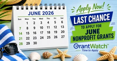 Promotional graphic for nonprofit grant applications. A desk calendar displaying “June 2026” sits on a beach-themed surface with a straw hat, tropical leaves, striped towel, sunglasses, seashells, and starfish. Beside the calendar, large text reads, “Apply Now! Last Chance to Apply for June Nonprofit Grants.” The logo and tagline “GrantWatch™ – Time to Apply” appear at the bottom.