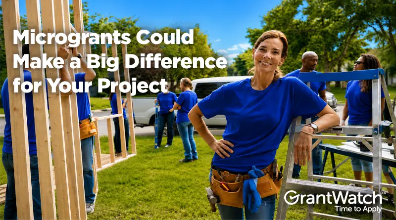 Volunteers wearing blue shirts work together on a community construction project outdoors. A woman in a tool belt stands beside building materials while text reads, “Microgrants Could Make a Big Difference for Your Project.” GrantWatch logo appears in the corner.