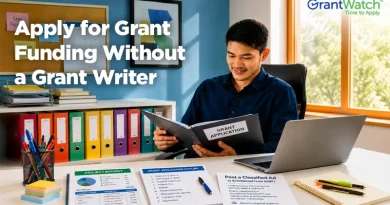 A person sits at a desk reviewing a grant application folder in a bright office. A laptop, project budget documents, grant application outline, office supplies, and colorful filing binders are arranged around the workspace. Large text reads, "Apply for Grant Funding Without a Grant Writer," with the GrantWatch logo displayed in the upper-right corner. The image conveys independent grant seeking, organization, and grant application preparation.