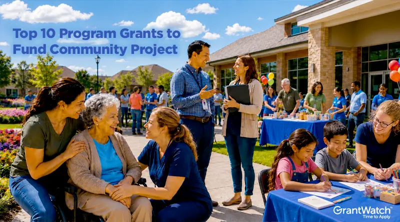 A vibrant community event takes place outside a large community center on a sunny day. Volunteers, families, seniors, and children gather for activities, conversations, and outreach programs. In the foreground, two caregivers support an elderly woman in a wheelchair while smiling and talking together. Nearby, children sit at a table drawing and coloring with a volunteer. Additional attendees mingle around activity booths decorated with colorful balloons. Overlay text reads, “Top 10 Program Grants to Fund Community Project,” and the GrantWatch logo appears in the bottom-right corner.