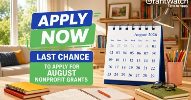 Graphic promoting nonprofit grant opportunities with the text "Apply Now: Last Chance to Apply for August Nonprofit Grants." A desktop calendar displays August 2026 beside notebooks, pens, glasses, and a desk lamp in a bright home office setting. The GrantWatch logo appears in the upper-right corner.