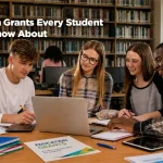 Four students collaborate around a laptop in a library, reviewing notes and educational materials. Bookshelves fill the background, while notebooks, tablets, and a document labeled "Education Grants" sit on the table. The image includes the headline "Education Grants Every Student Should Know About" and the GrantWatch logo in the upper corner.
